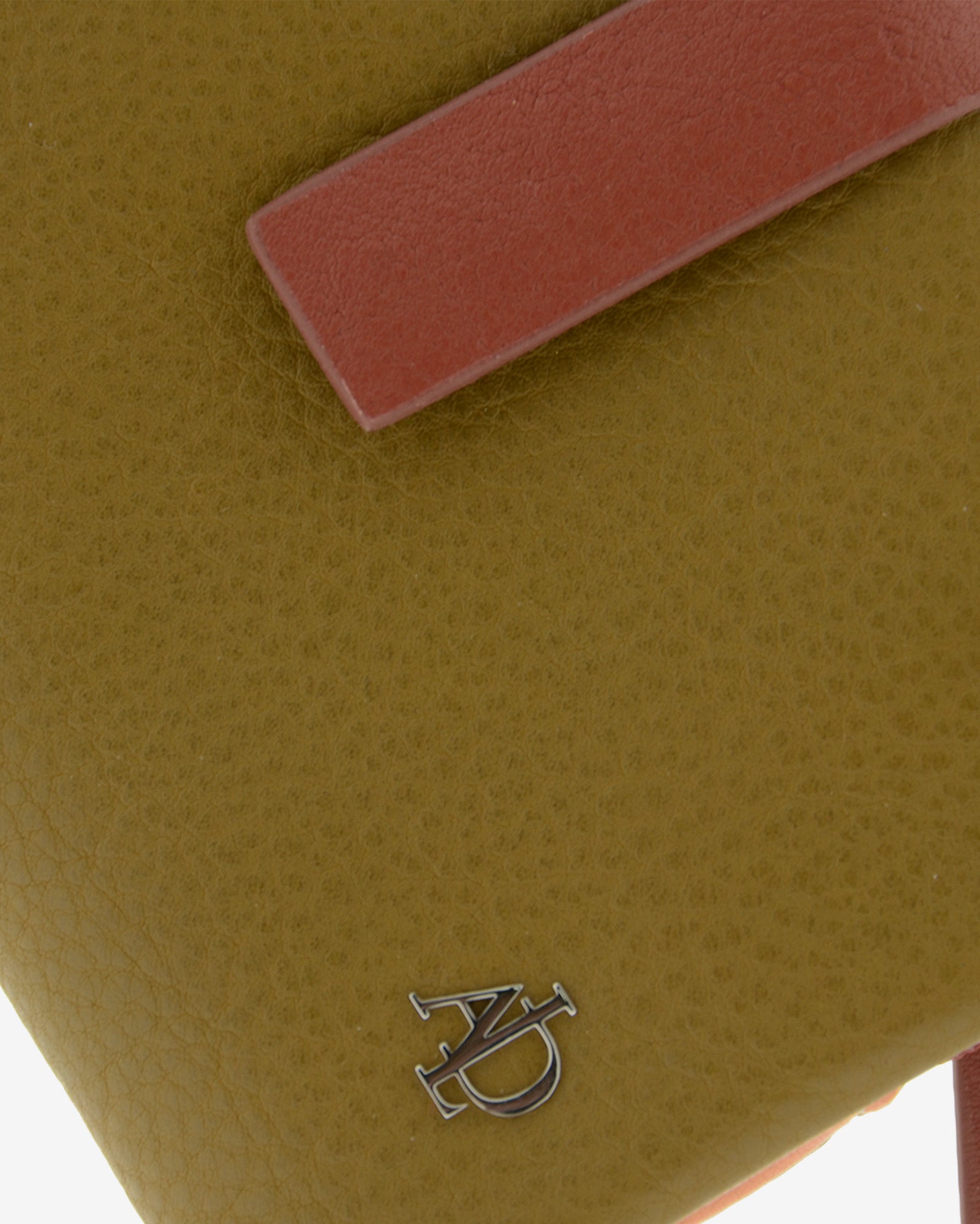 Detalle del logo metálico y la textura de la piel en la cartera pequeña de mujer Brisa color Ámbar Ébano.