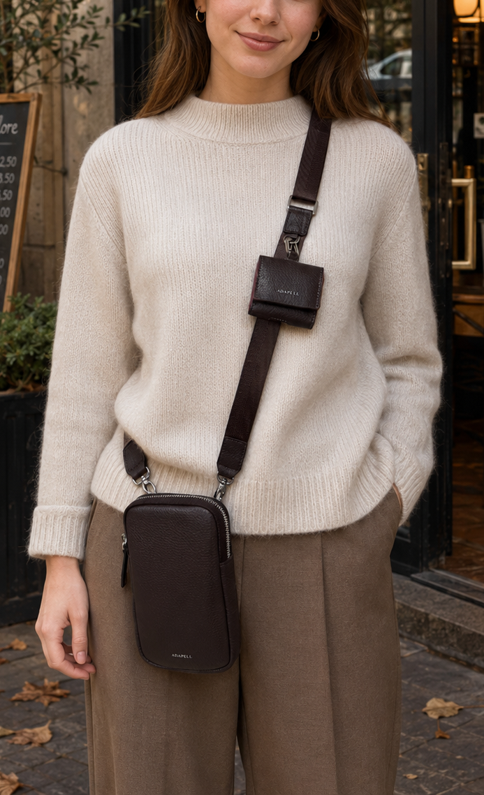 Mujer joven con funda para auriculares Nexo 8093 en color chocolate acoplada a la bandolera de un bolso Nexo negro y fondo exterior cafetería