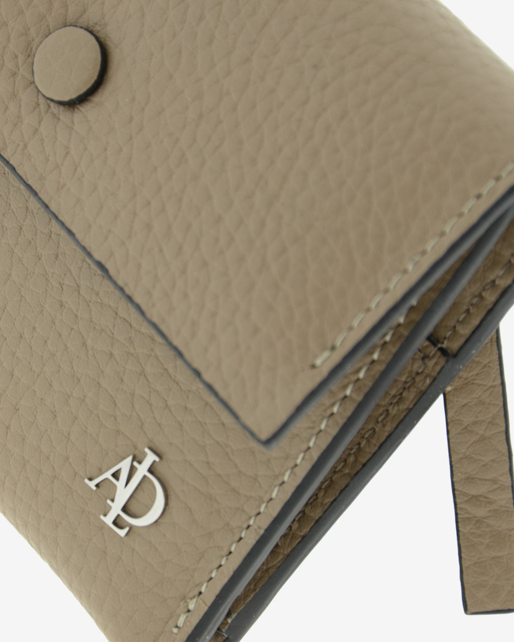 Detalle frontal de la cartera pequeña Nude en color Topo con solapa, botón, costuras, textura de la piel y logo Adapell.