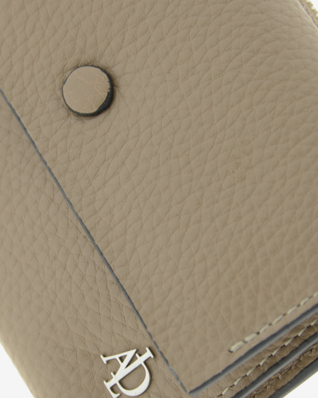 Detalle de la solapa con botón a presión, la textura de la piel y el logo metálico Adapell de la cartera Nude en color Topo.