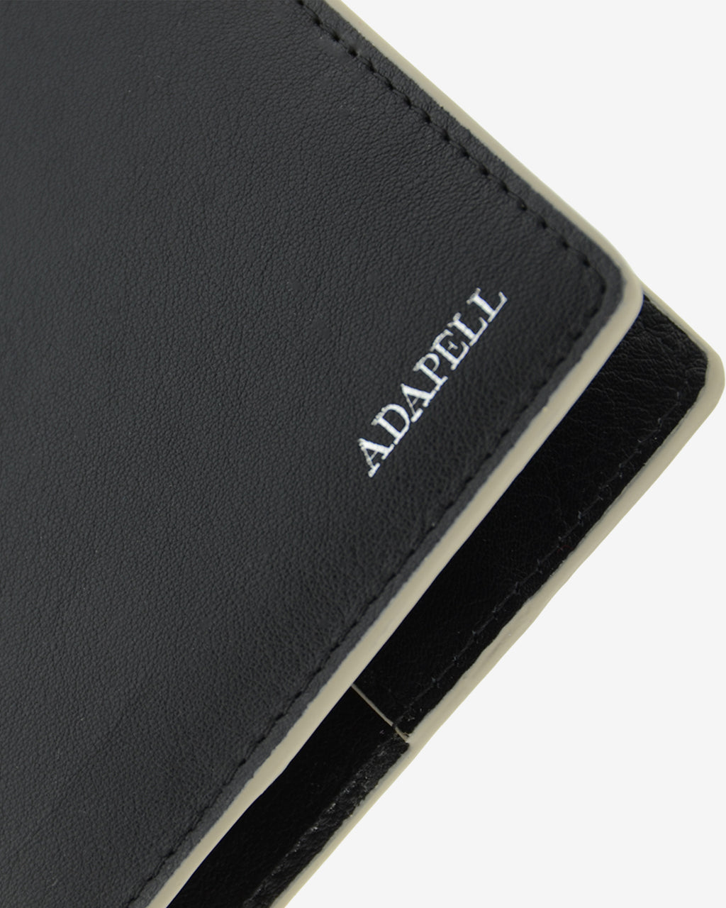 Funda pasaporte en piel auténtica muy suave de color negro y cantos en gris, con protección RFID, y logo plateado Adapell, vista detalle de piel