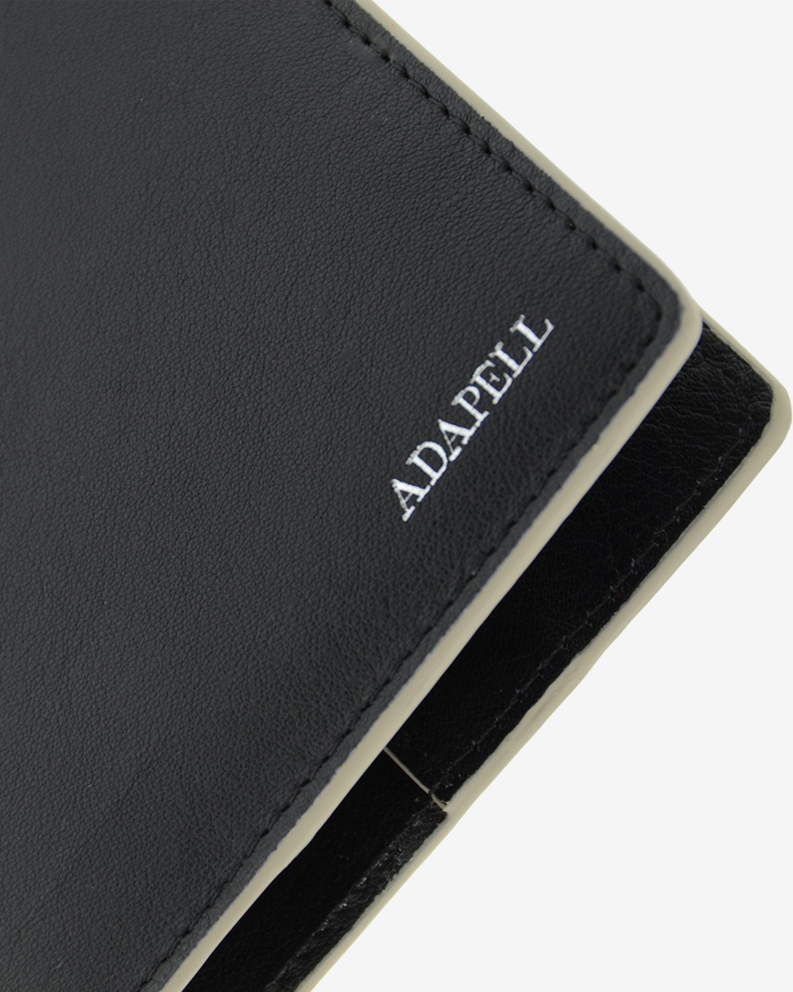 Funda pasaporte en piel auténtica muy suave de color negro y cantos en gris, con protección RFID, y logo plateado Adapell, vista detalle de piel