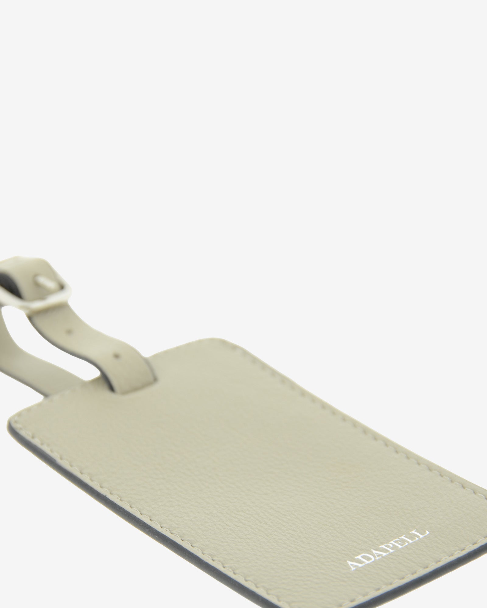 Tag identificador maleta con cierre de hebilla, ref. 8088-12, en piel de color ice stone y cantos en negro, con logo Adapell, vista detalle de piel, logo y acabados