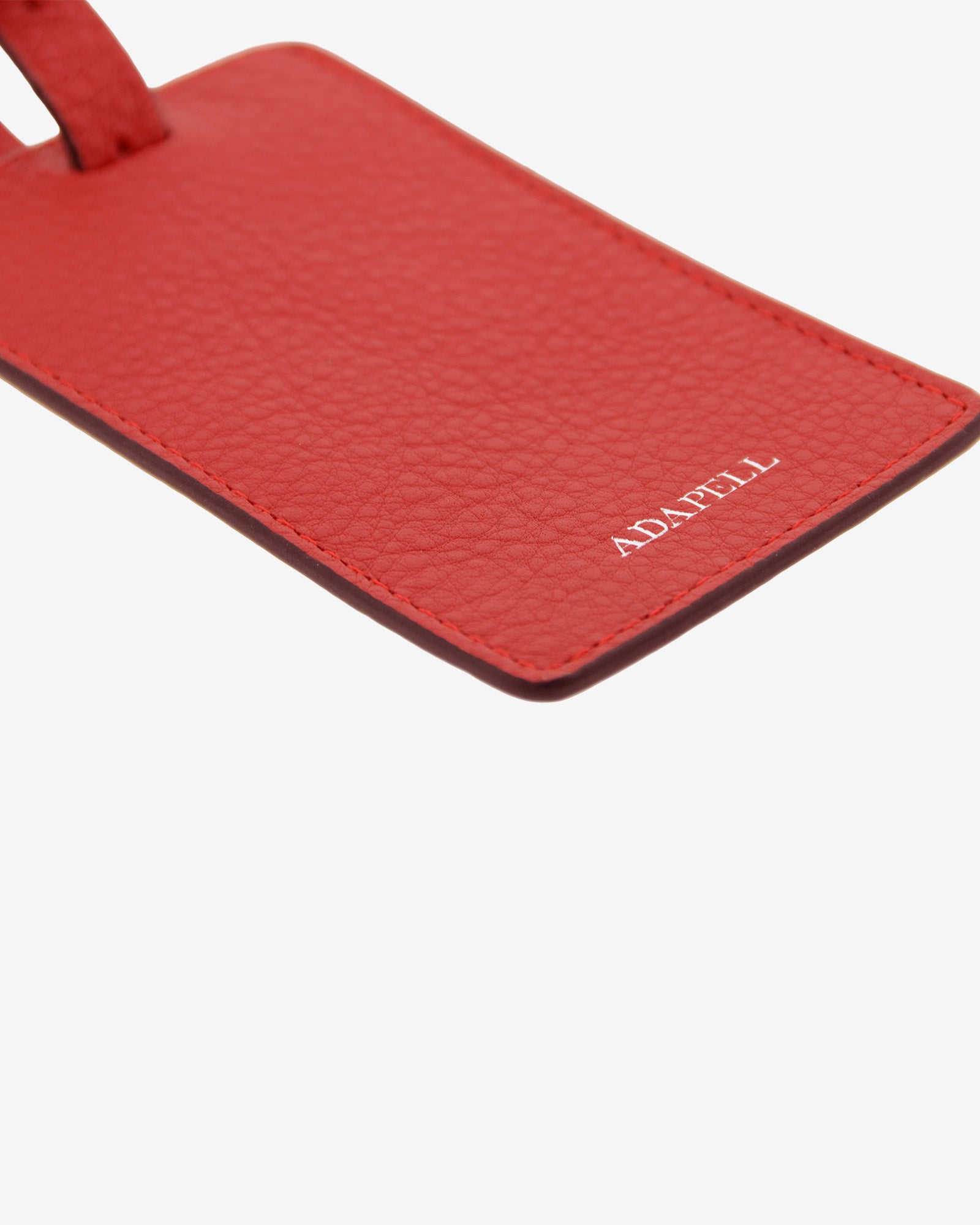 Tag identificador maleta con cierre de hebilla, ref. 8088-3, en piel de color rojo y cantos en negro, con logo Adapell, vista detalle de piel y acabados